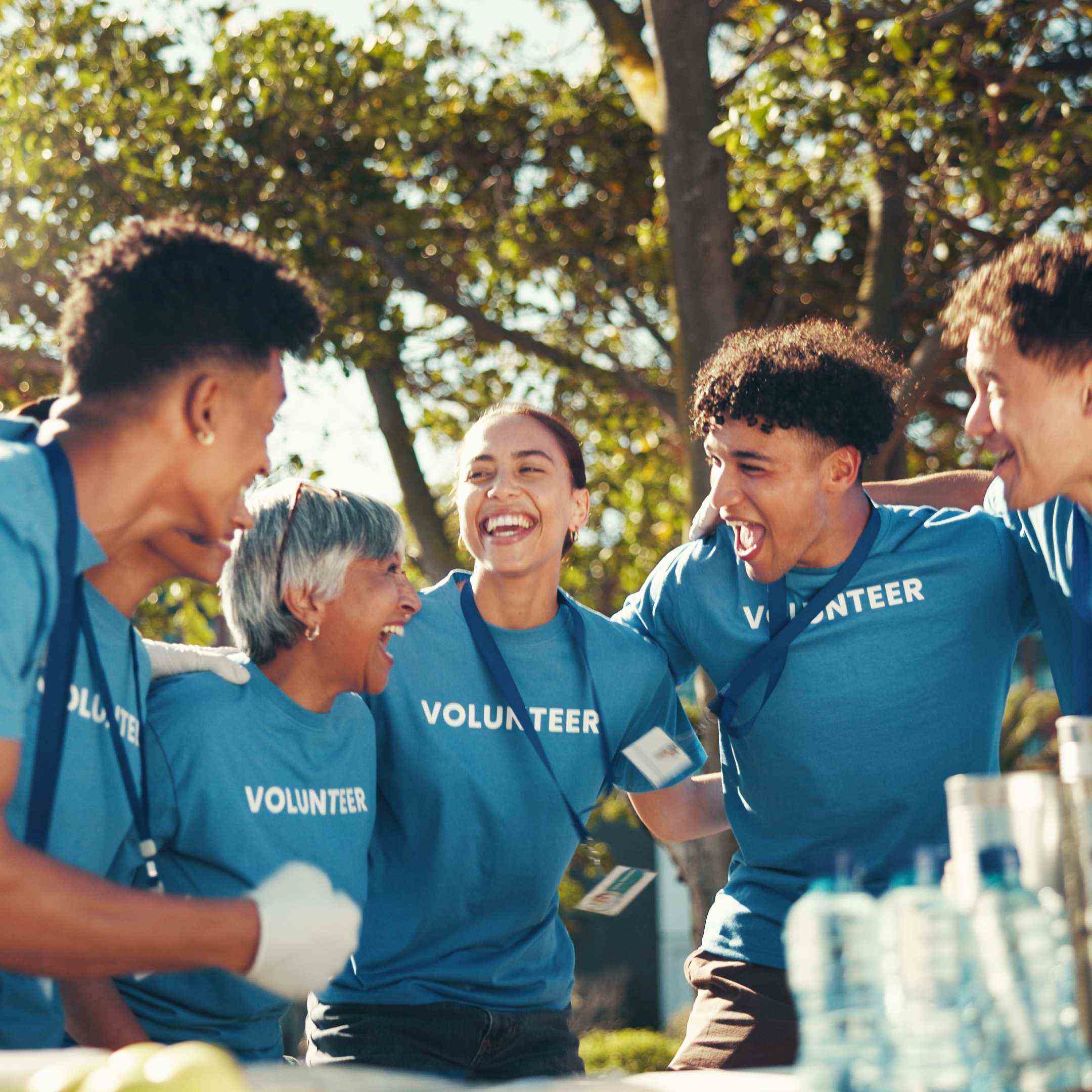 Group of volunteers in blue 'VOLUNTEER' shirts laughing outdoors.