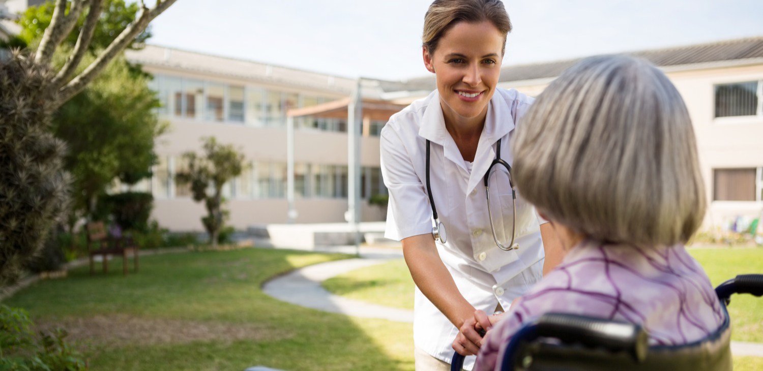 Nurse assisting an elderly woman in a wheelchair outdoors.