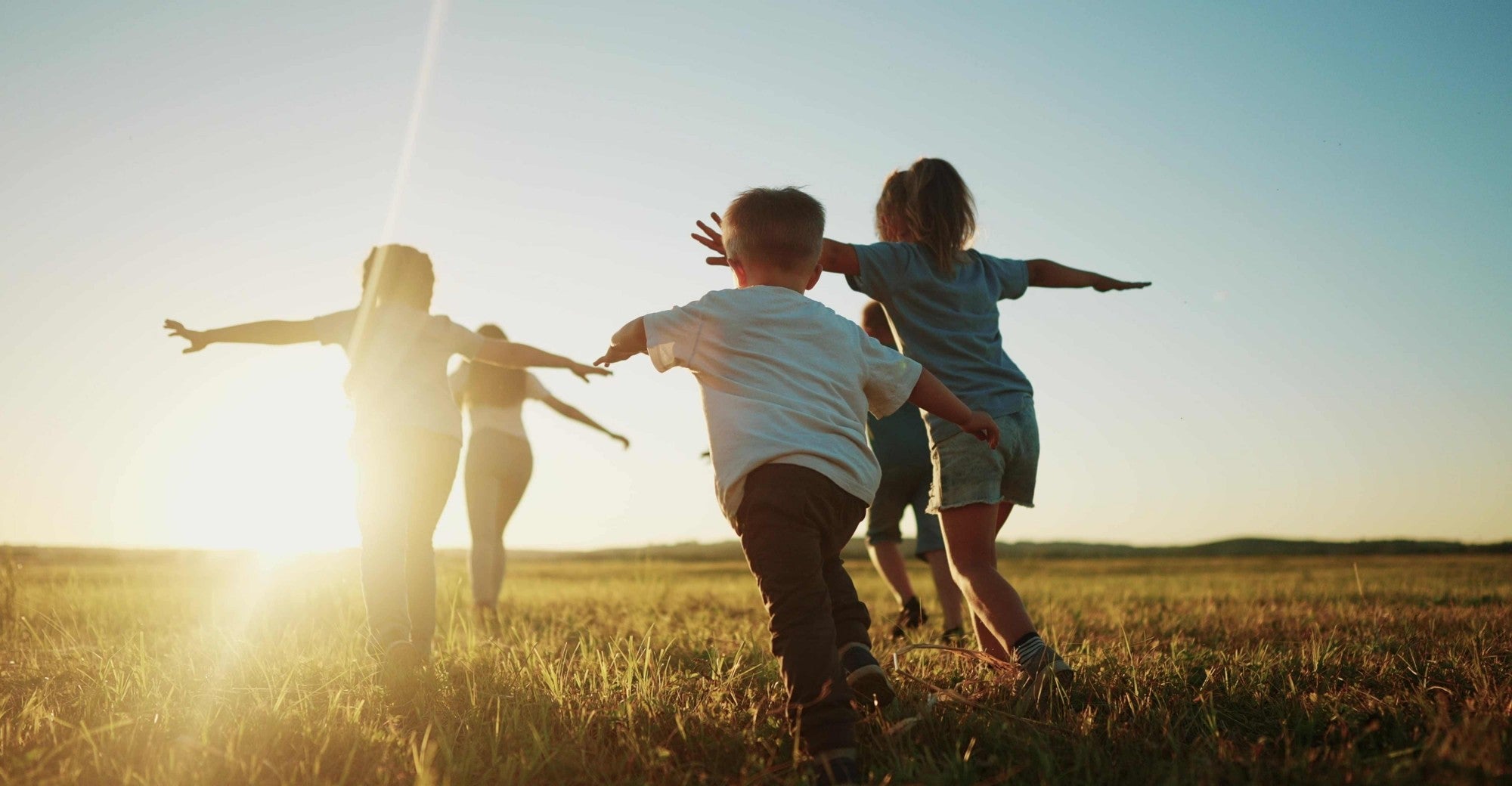 Family of five standing in a field with arms outstretched, enjoying a sunny day.