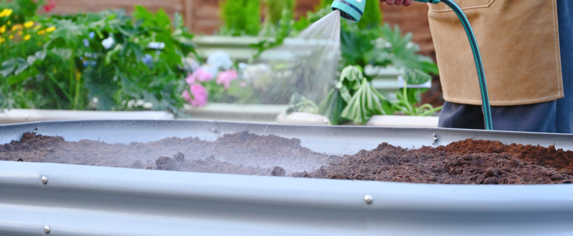 Person watering a raised garden bed with a hose